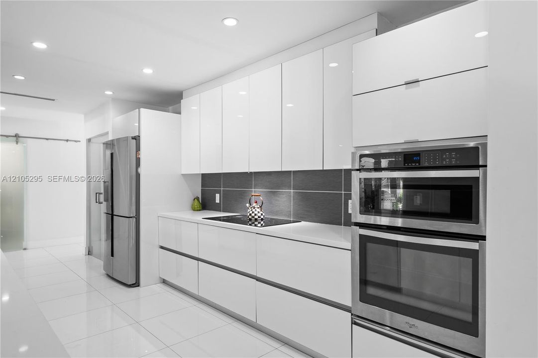 Kitchen featuring high-gloss white cabinetry, stainless steel built-in double ovens, white solid-surface countertops, charcoal-toned tile backsplash, and polished tile flooring