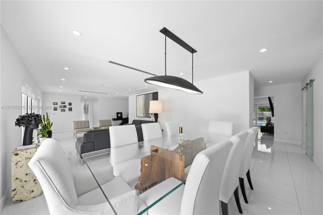 Open-concept interior featuring large-format tile flooring, recessed lighting, and a modern black linear pendant light fixture, complemented by a frosted glass sliding barn door
