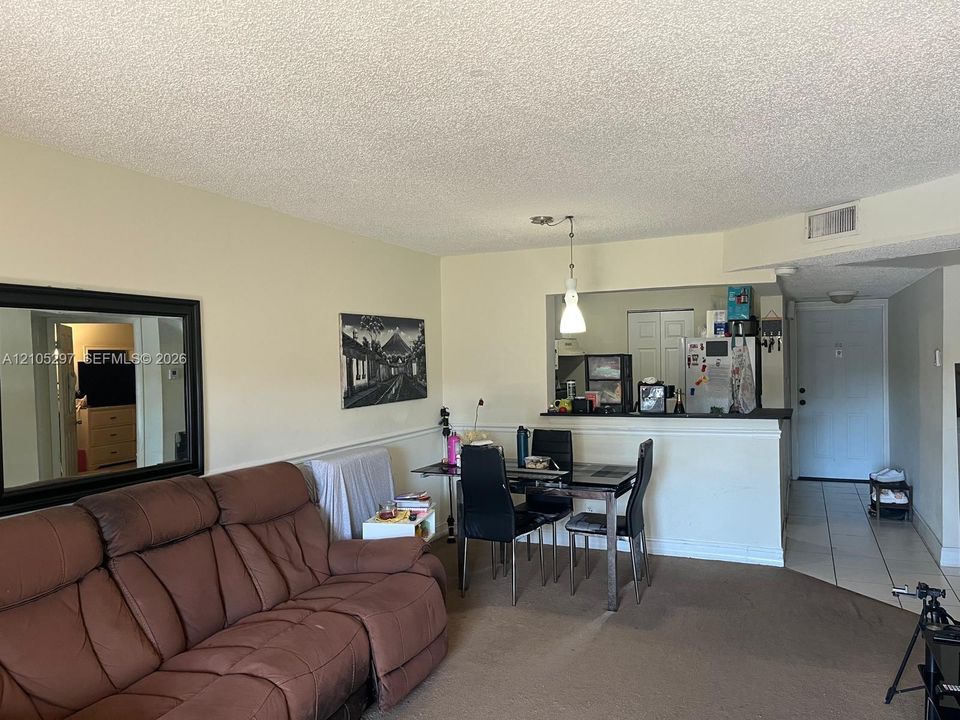 Open concept living area with carpet flooring, a pass-through kitchen with a breakfast bar, and tile flooring at the entry