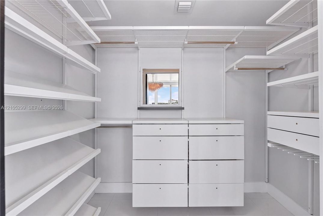Integrated closet system with extensive shelving, built-in drawer units, hanging rods, and an overhead window