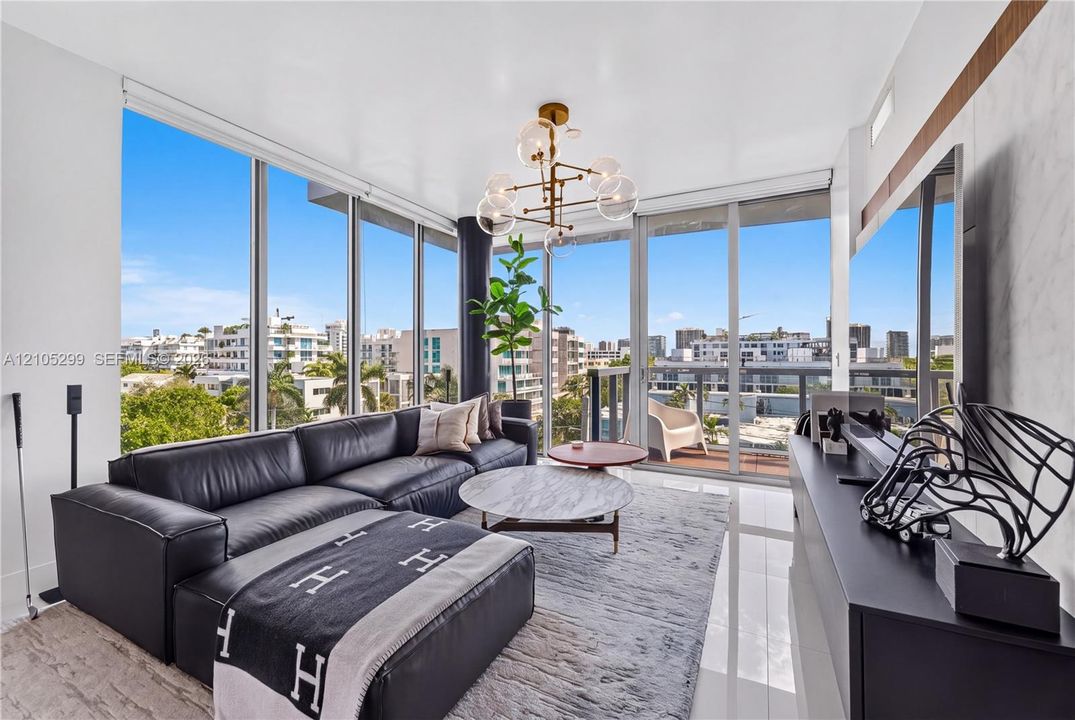 Floor-to-ceiling windows, polished tile flooring, modern chandelier, built-in media console, and a private balcony
