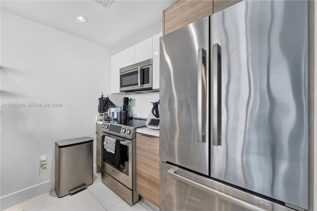 Stainless steel appliances, built-in microwave, wood-finish cabinetry, white upper cabinets, and recessed lighting