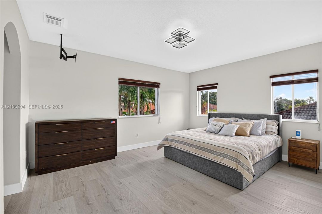 Spacious room featuring wood-finish flooring, multi-pane windows with horizontal blinds, an arched entryway, and a geometric flush-mount light fixture