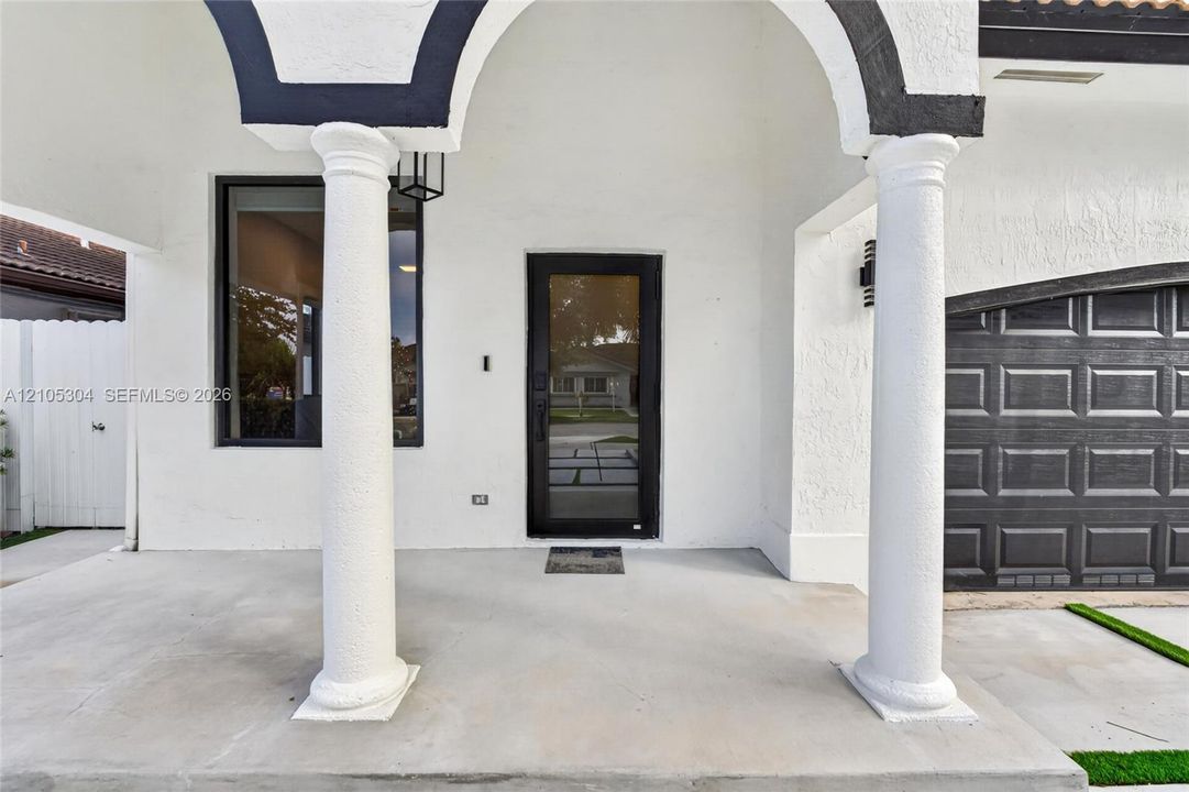 Covered entryway featuring structural columns, stucco exterior finish, full-glass front door, and paneled garage door