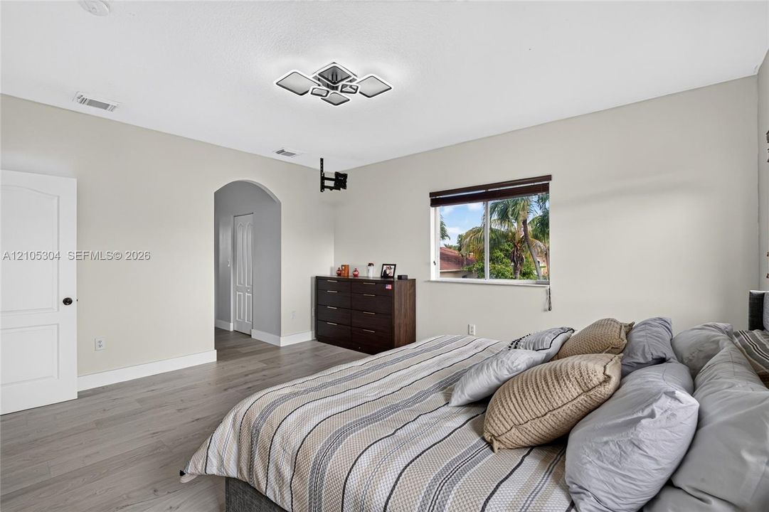 Wood-finish flooring, geometric ceiling lighting, arched entryway, and single-hung window with dark window treatments