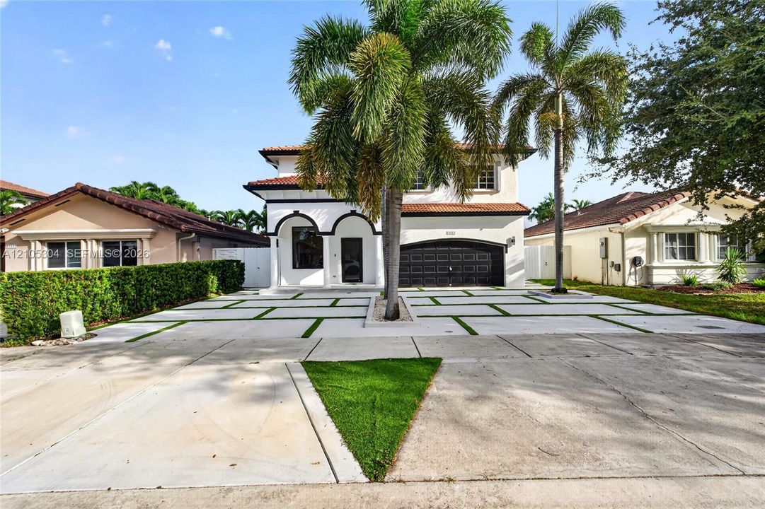 Two-story exterior featuring a clay tile roof, arched entryway, multi-panel garage door, and a geometric concrete paver driveway with turf accents