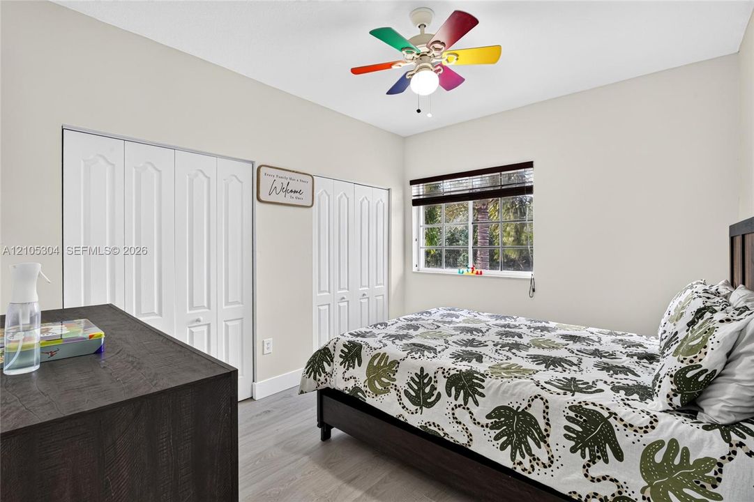 Neutral-toned walls, wood-finish flooring, dual bi-fold closet doors, and a multi-colored ceiling fan with integrated light fixture
