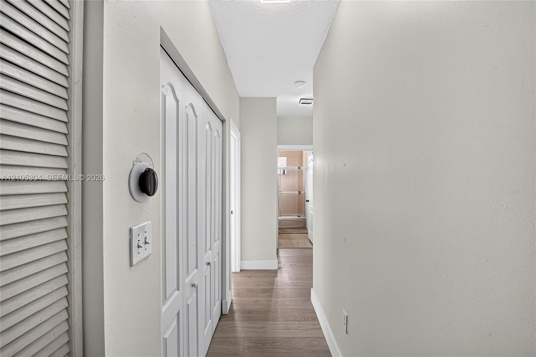 Hallway featuring wood-finish flooring, white louvered closet doors, and a double-panel interior closet door