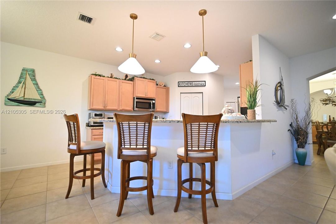 Kitchen with light-toned cabinetry, stainless steel microwave, recessed lighting, and two pendant lights over a countertop bar