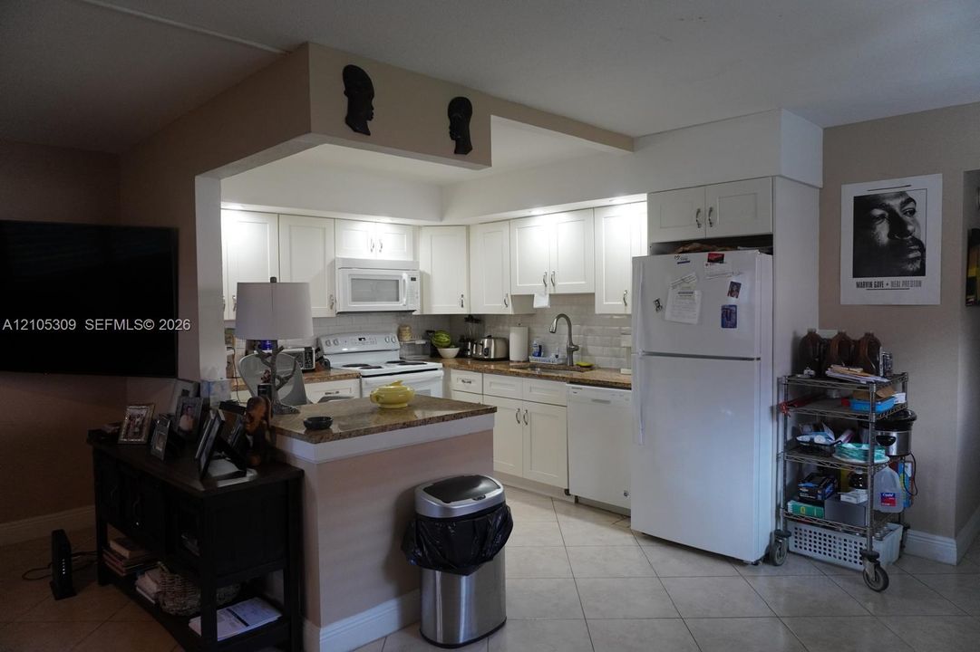Kitchen featuring white shaker-style cabinetry, stone-finish countertops, tiled backsplash, and built-in appliances including a dishwasher and microwave