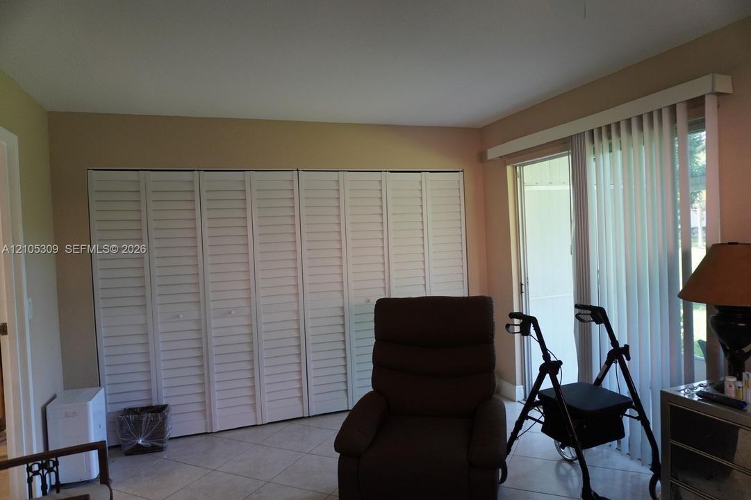 Full-wall louvered closet doors, neutral wall finish, ceramic tile flooring, and vertical blinds covering the sliding glass door