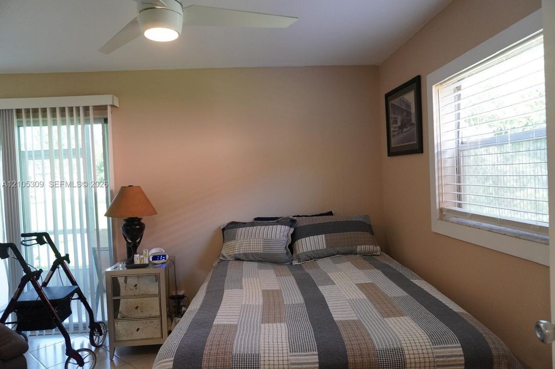 Room featuring neutral wall paint, a ceiling-mounted light fixture with fan, and a sliding glass door with vertical blinds