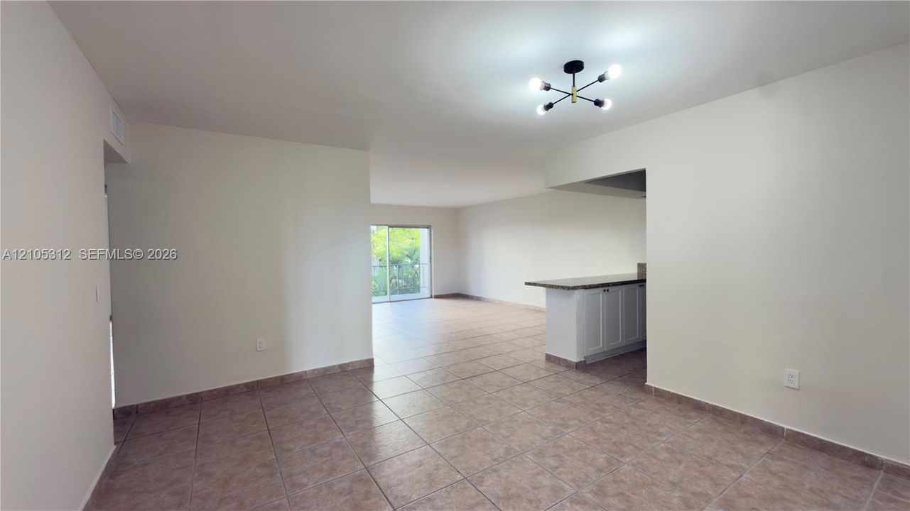 Neutral-toned interior featuring ceramic tile flooring, a multi-arm modern ceiling fixture, and a built-in kitchen peninsula with stone-finish countertop