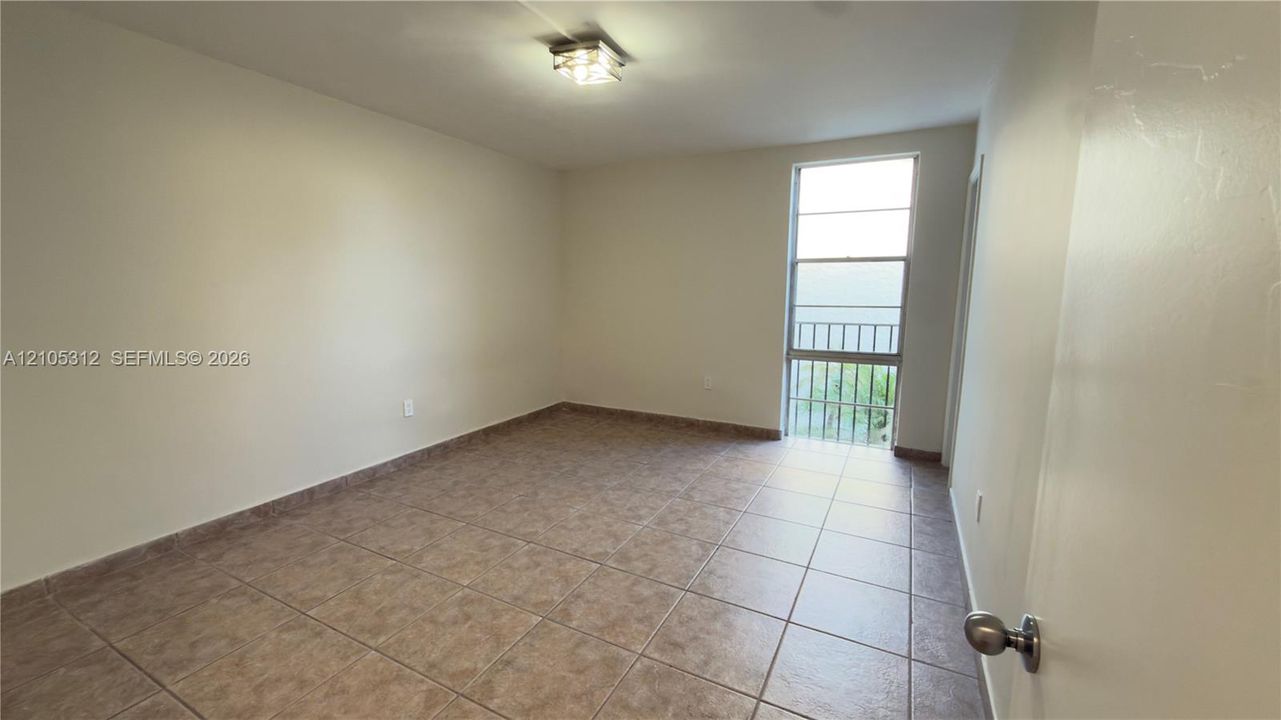 Neutral-toned interior space featuring large-format ceramic tile flooring, a rectangular multi-pane window with a metal security grate, and a square-profile ceiling-mounted light fixture
