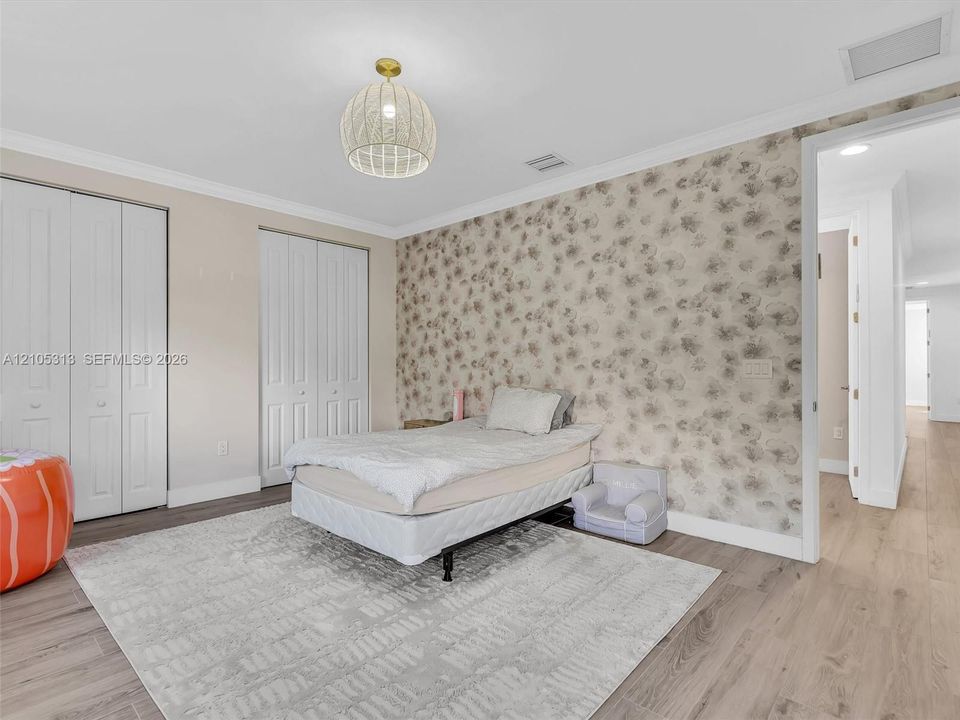 Room featuring wood-finish flooring, decorative patterned wall covering, double-door closets, and a pendant light fixture with a woven shade