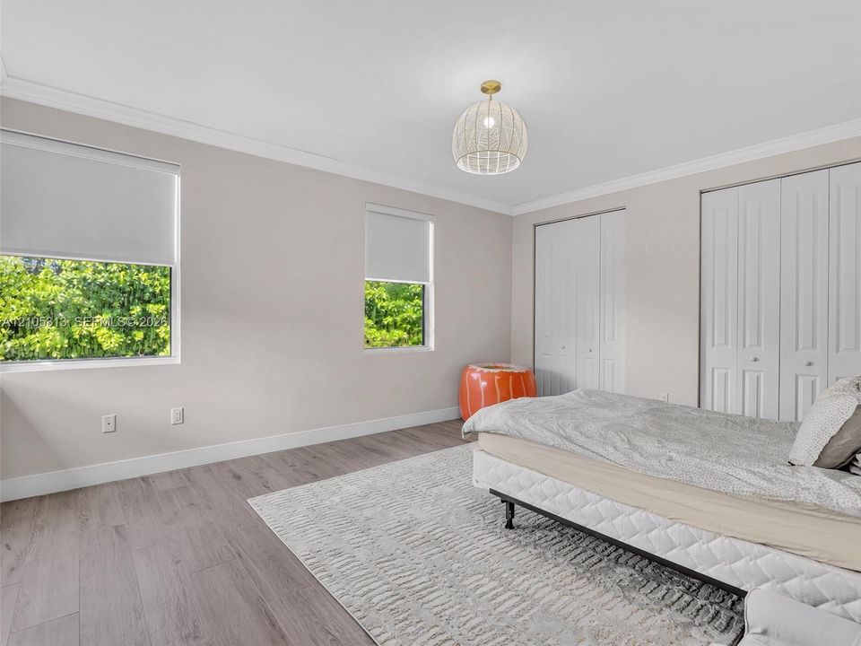 Room featuring wood-finish flooring, dual windows with roller shades, white bifold closet doors, and a woven dome-style ceiling light fixture