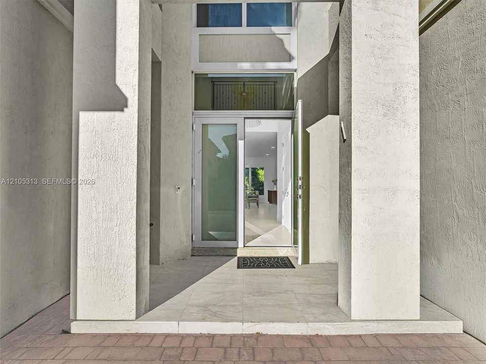 Covered entryway featuring dual structural columns, stone-finish porch flooring, and a multi-pane glass door with a transom window