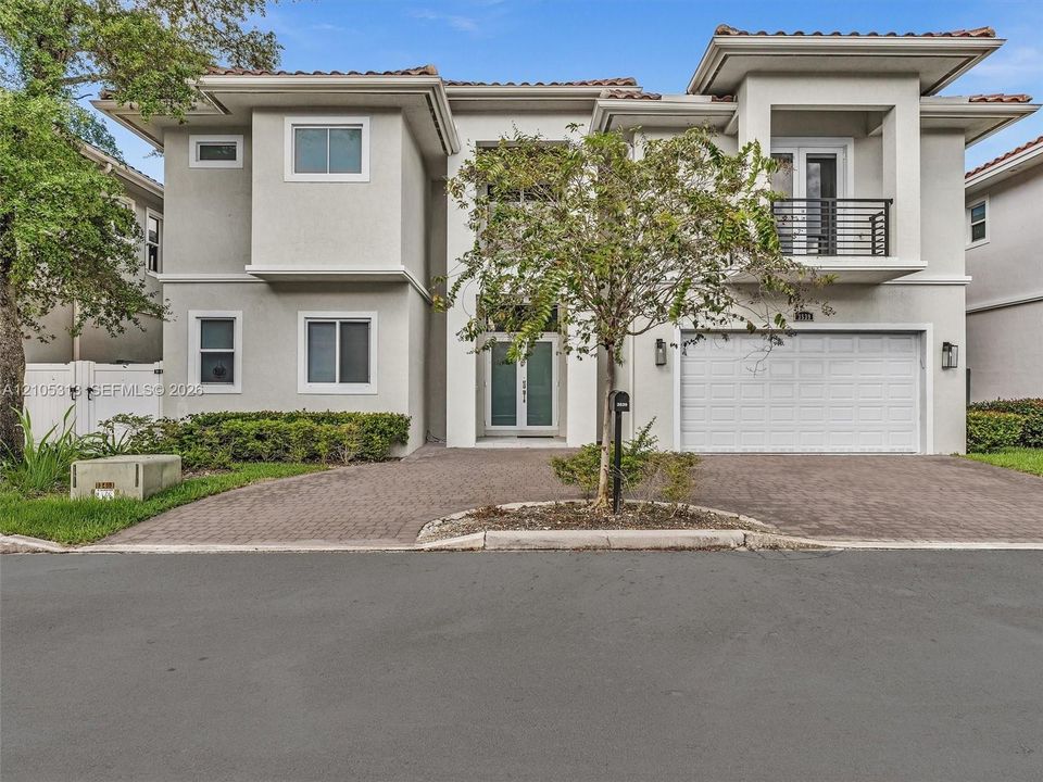 Two-story stucco exterior featuring a paved driveway, integrated two-car garage, upper-level balcony with metal railing, and double-entry doors