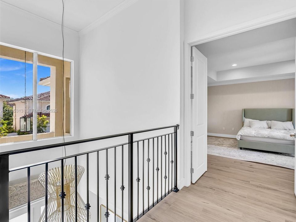 Landing area featuring wood-finish flooring, a decorative metal railing, crown molding, and a suspended metal pendant light fixture