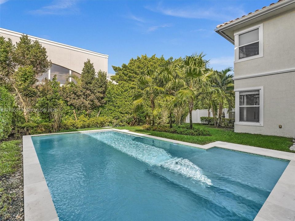 Private backyard featuring an in-ground swimming pool with a stone paver surround, manicured lawn, and mature perimeter landscaping