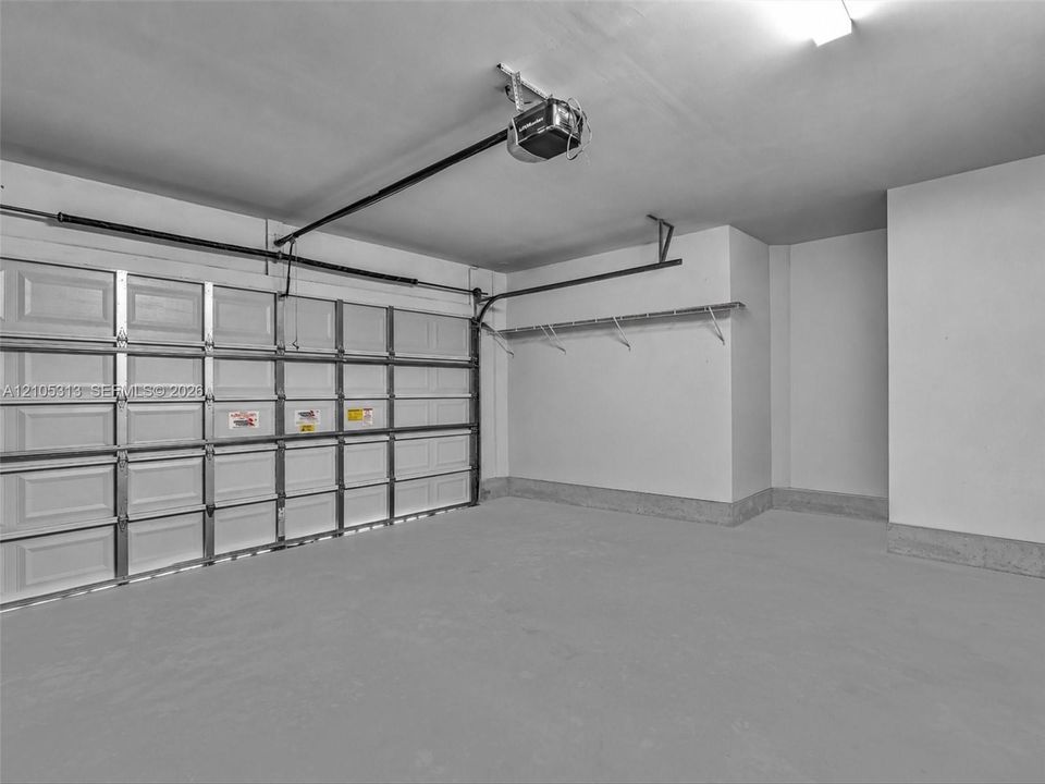 Two-car garage featuring a sectional door, concrete flooring, automatic door opener, and wall-mounted shelving