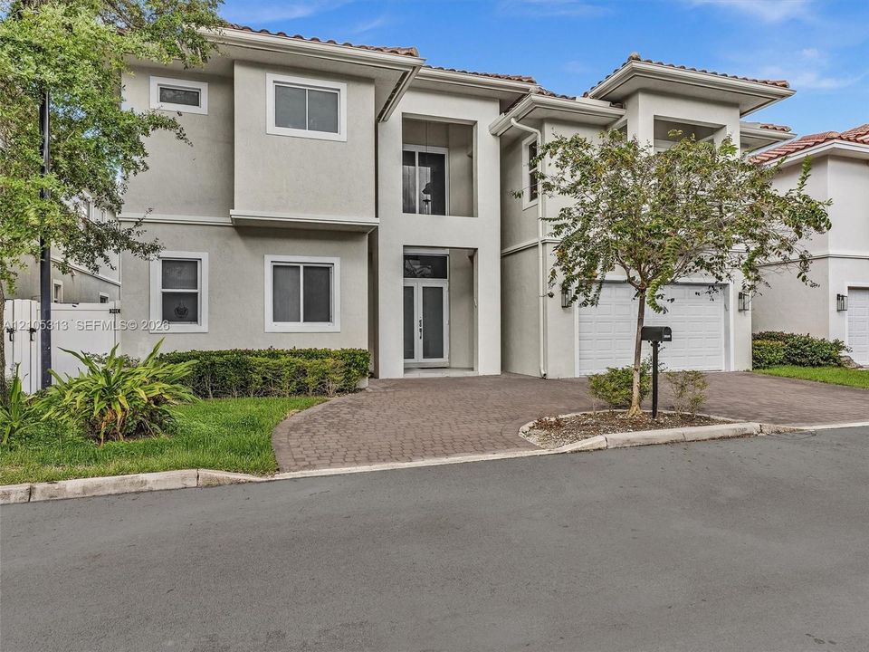 Two-story residence featuring a tile roof, stucco exterior, paver driveway, covered entryway, and an attached two-car garage