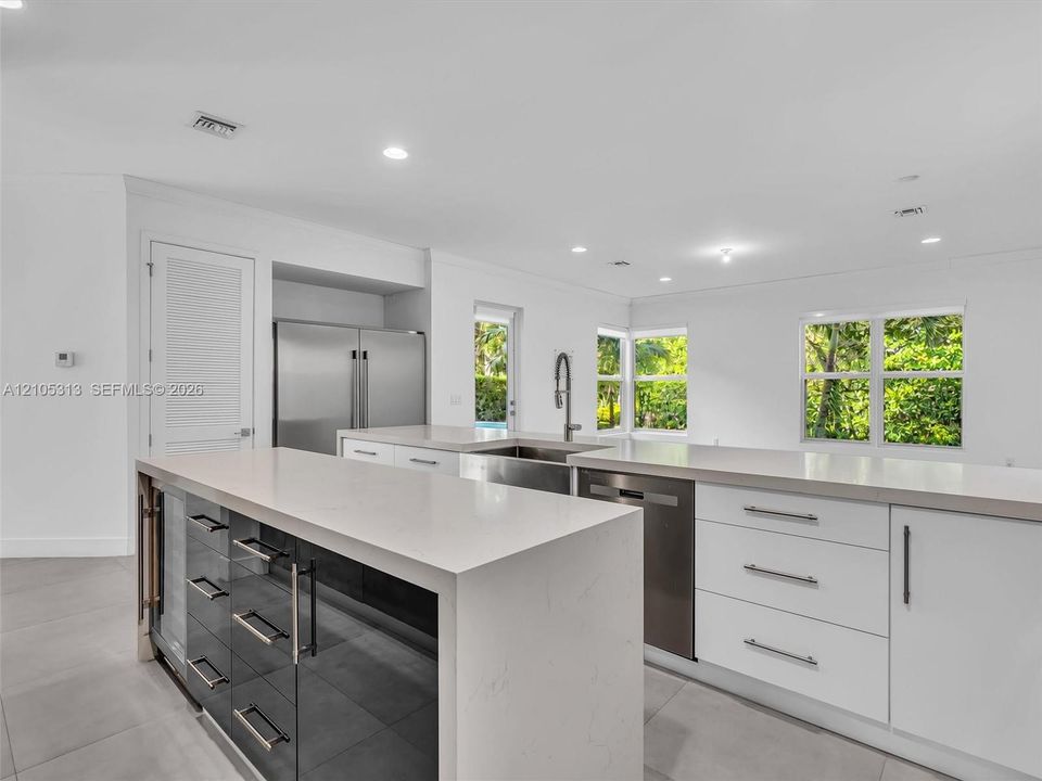 Kitchen featuring a waterfall-edge stone countertop, custom cabinetry with integrated wine refrigeration, stainless steel appliances, and large-format tile flooring