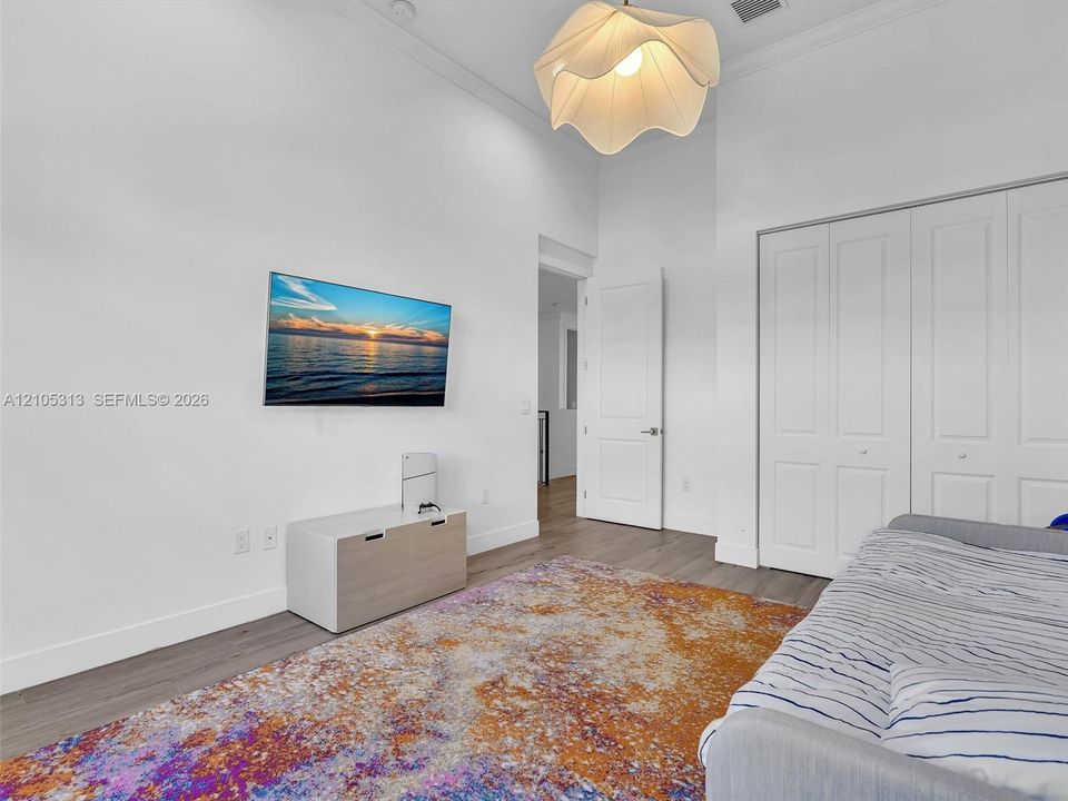 High ceilings, wood-finish flooring, white multi-panel doors, floor-to-ceiling built-in closet with paneling, and architectural pendant lighting