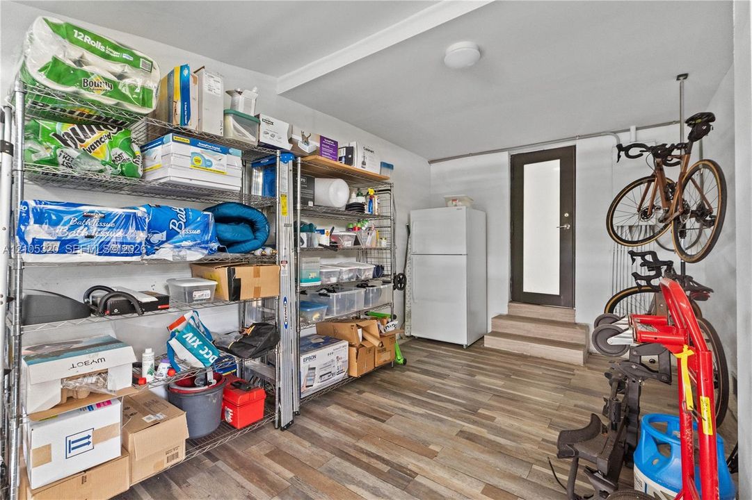 Wood-finish flooring with a white refrigerator and a dark-framed door with frosted glass