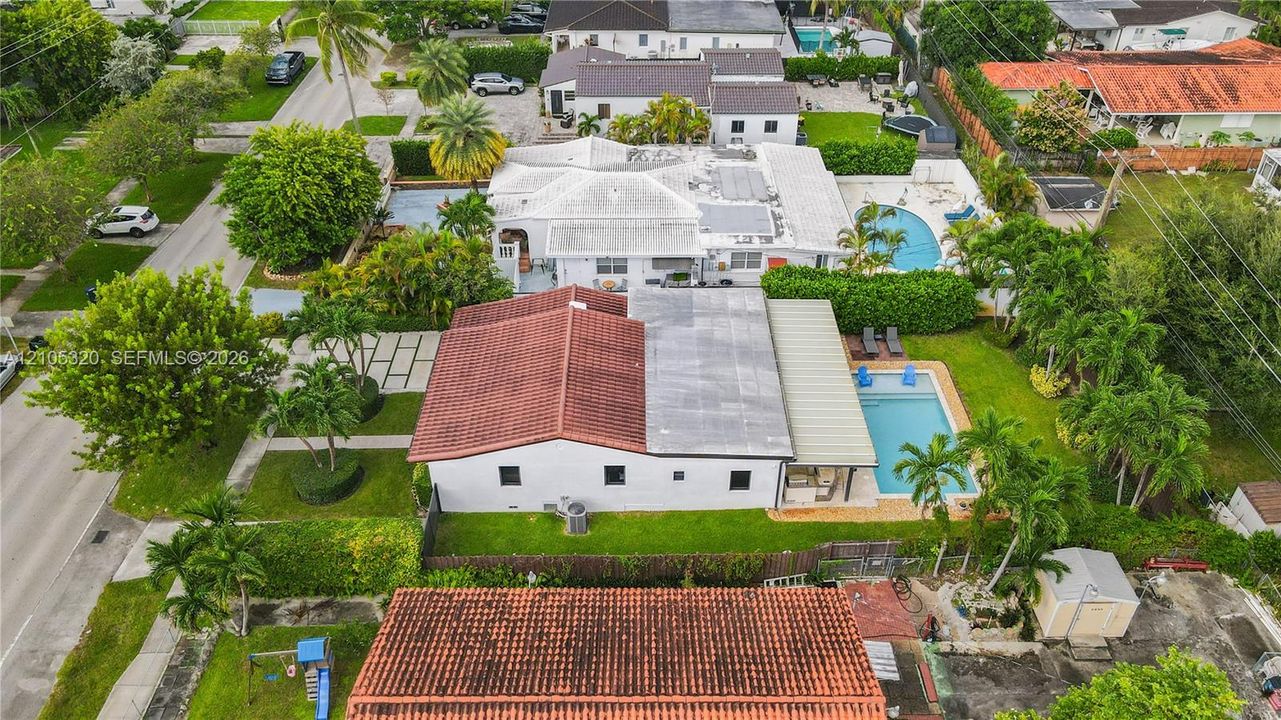 Red tile roof, white exterior, manicured lawn, inground swimming pool, and mature palm trees