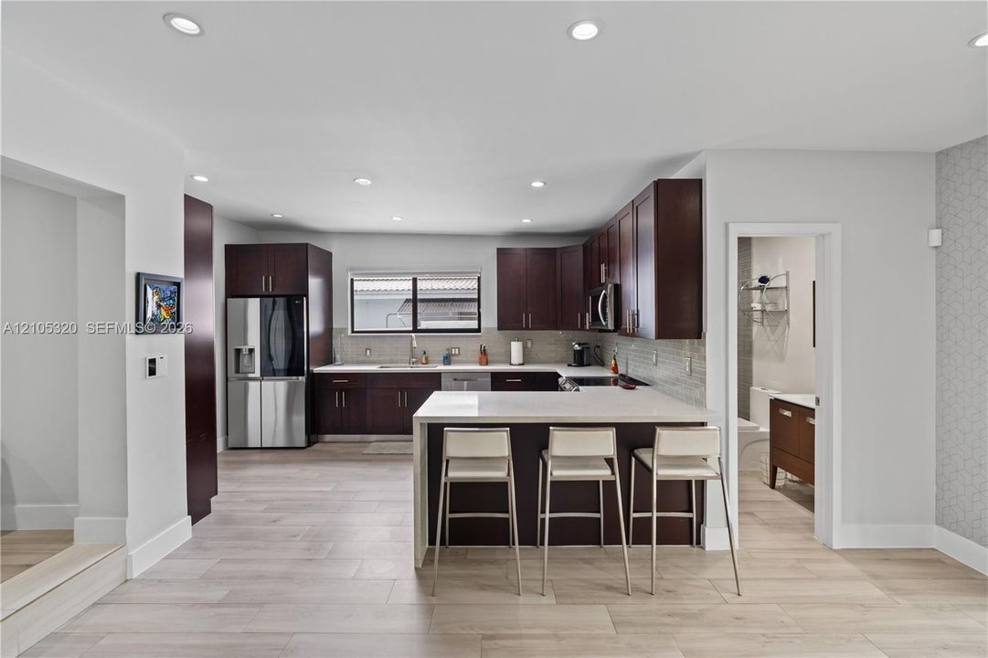 Contemporary kitchen featuring dark wood cabinetry, stainless steel appliances, light countertops, and a full-height tile backsplash