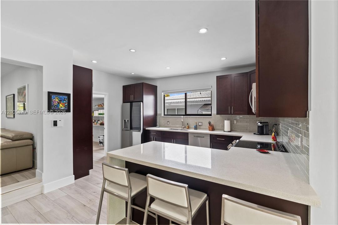 Modern kitchen featuring dark wood cabinetry, stainless steel appliances, a white stone countertop, a tile backsplash, and recessed lighting