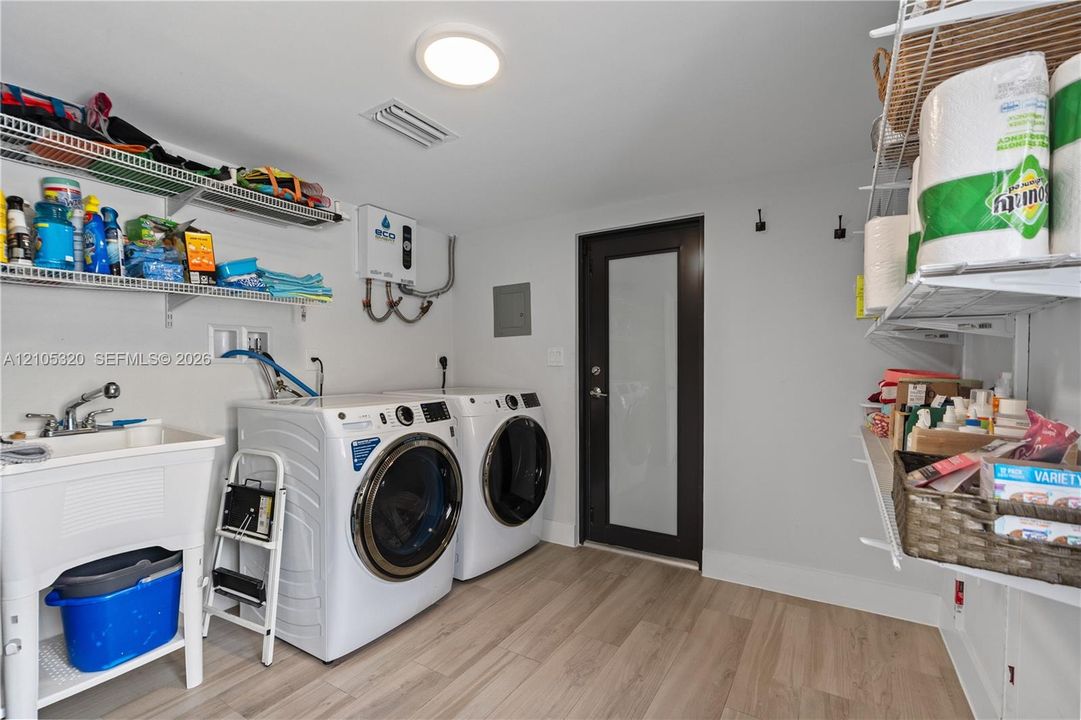 Laundry area with wood-finish flooring, a utility sink, and wall-mounted shelving