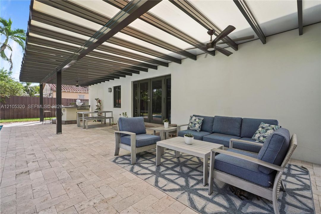 Expansive paver patio with a covered pergola featuring an integrated ceiling fan