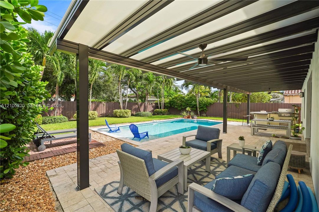Expansive outdoor living area featuring a covered patio, ceiling fan, inground swimming pool, and dedicated outdoor kitchen space