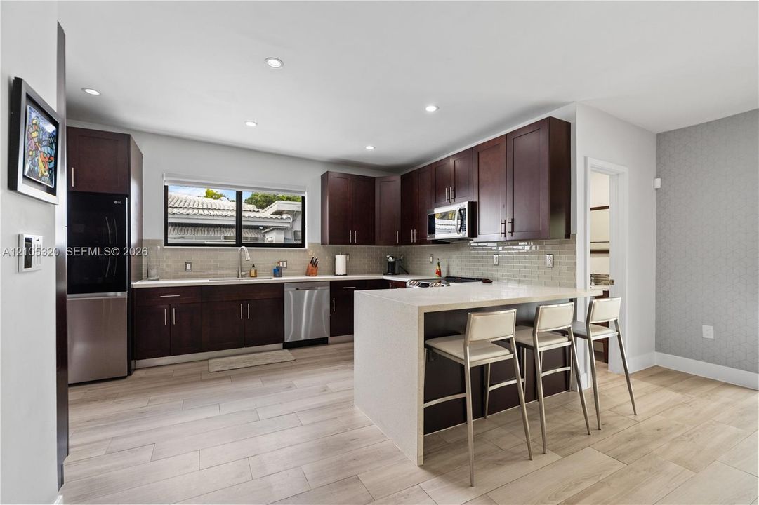 Modern kitchen with wood-finish flooring, dark wood cabinetry, white countertops, and stainless steel appliances