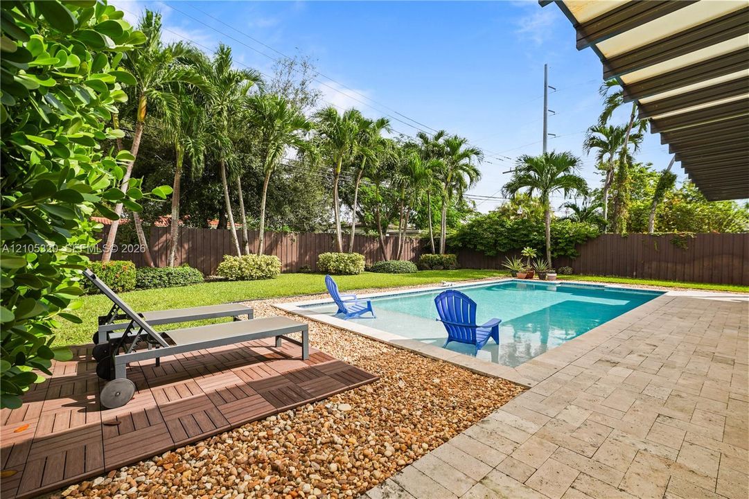 Rectangular swimming pool with integrated seating ledge, surrounded by a paved patio and lush green lawn
