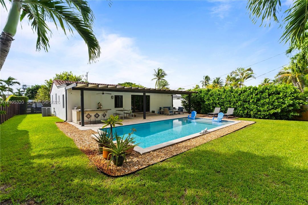 Rectangular swimming pool with a gravel surround, covered patio with a built-in outdoor kitchen, stucco exterior, and a tile roof