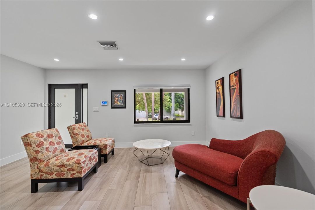 Recessed lighting illuminating the room, light-toned wood-finish flooring, and a window with black trim