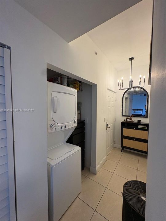 Hallway featuring a built-in laundry area with stacked appliances, tiled flooring, and a decorative light fixture