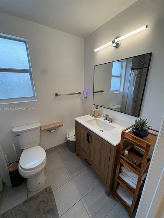 White vanity with integrated sink, modern black-framed mirror, contemporary wall-mounted light fixture, and large format tile flooring