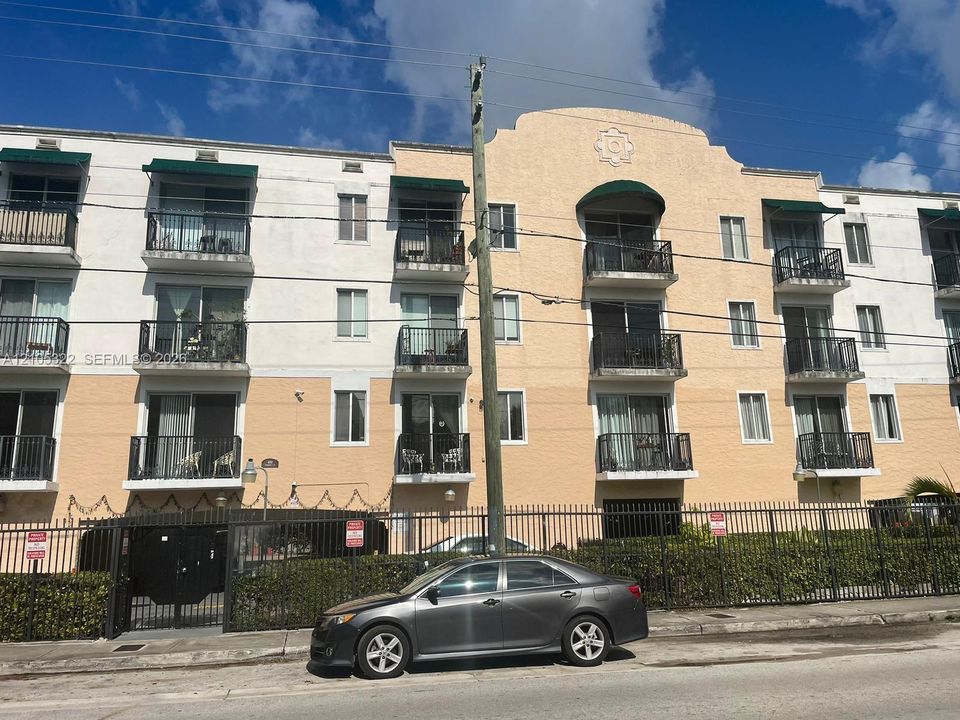 Multi-story building featuring balconies with wrought iron railings, individual green awnings, and a secured entrance gate