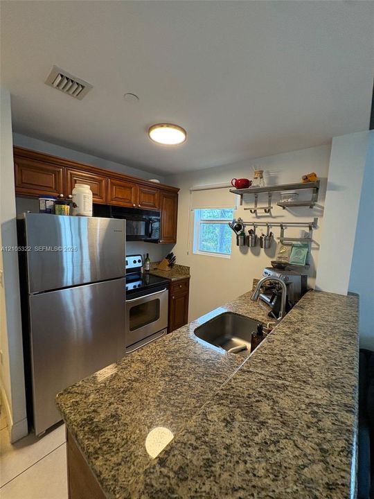 Granite-finish countertops, stainless steel appliances, wood-finish cabinetry, stainless steel sink, and a built-in oven