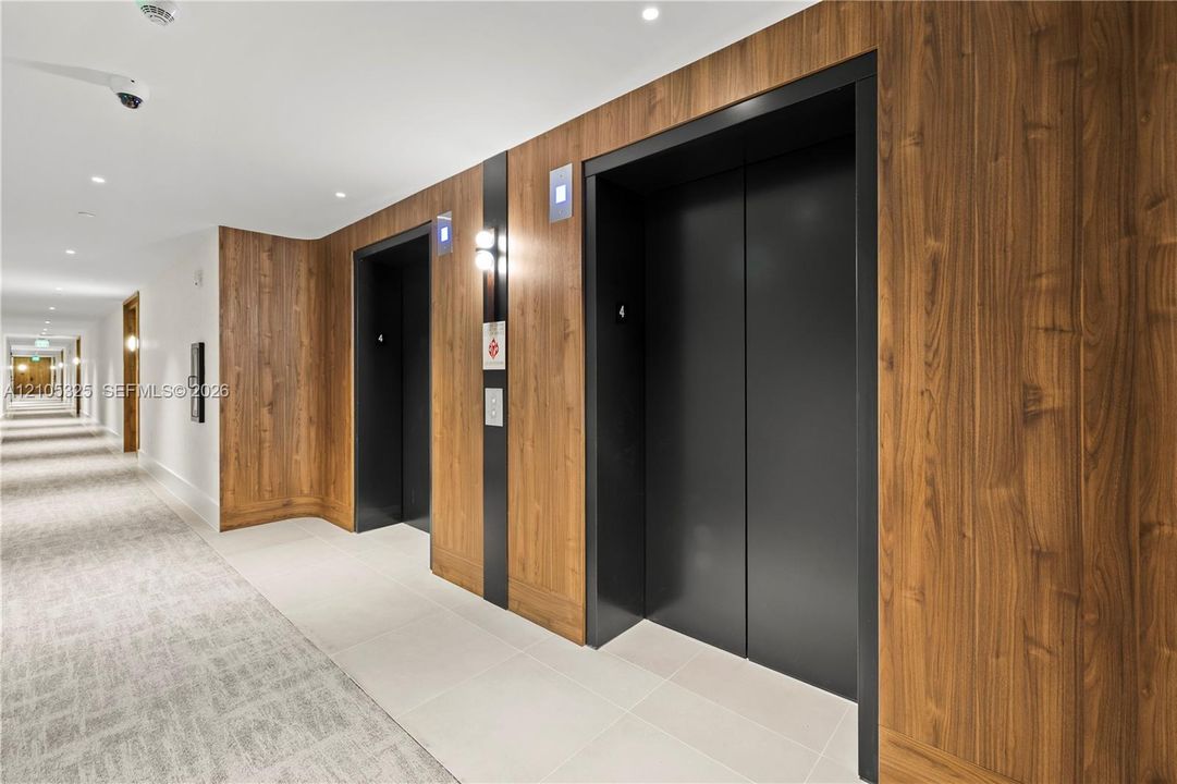 Hallway featuring wood-finish wall panels, recessed lighting, and elevators with black doors