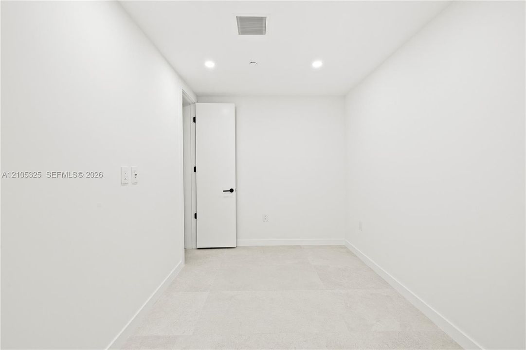 Recessed ceiling lighting, white walls, light-colored tile flooring, solid core door with matte black hardware
