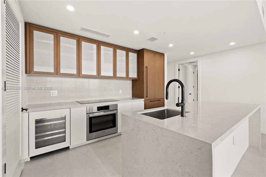 Modern kitchen featuring white quartz countertops, stainless steel dual wall ovens with integrated microwave, wine refrigerator, and a professional-style pull-down faucet