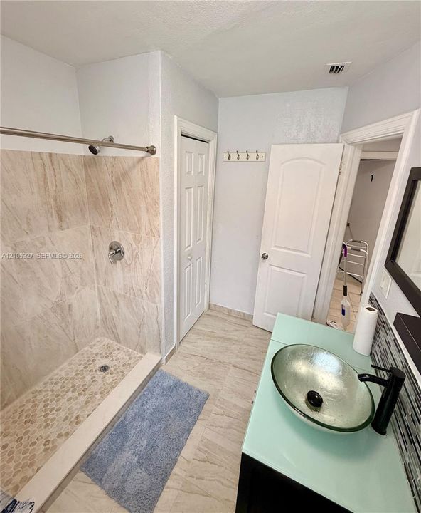 Walk-in shower with natural stone-look wall tiles and a pebble-tiled floor