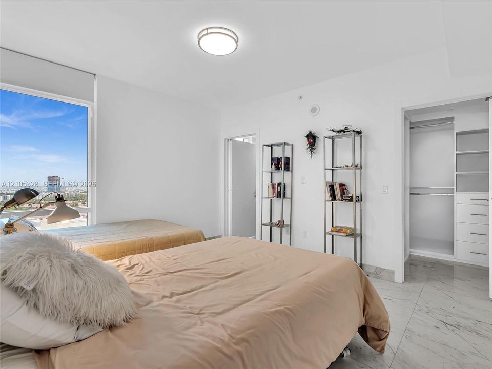 Bright and elegantly appointed interior featuring an expansive window that fills the space with natural light, a custom built-in closet organization system, polished stone flooring, crisp white walls, and recessed ceiling lighting.