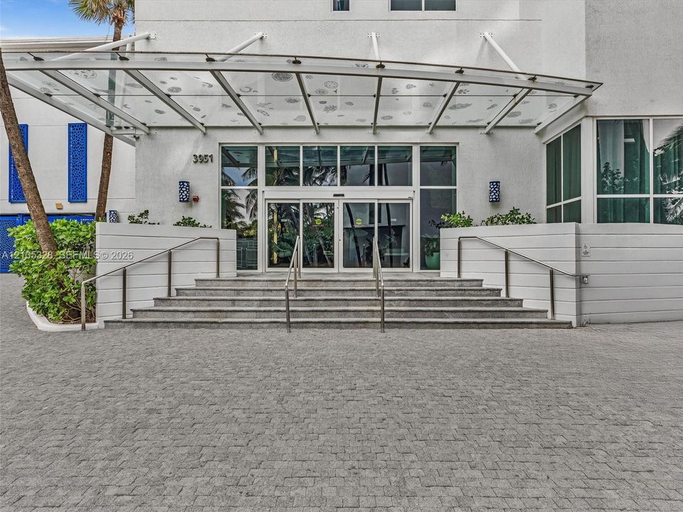 Elegant building entrance featuring a contemporary glass canopy, beautifully paved entryway, and sleek stainless steel railings, creating a sophisticated arrival experience.