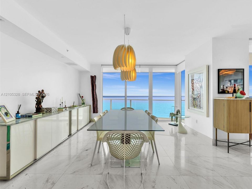 Elegant dining area featuring floor-to-ceiling glass doors and windows, large-format tile flooring, contemporary pendant lighting, and a glass-top dining table.